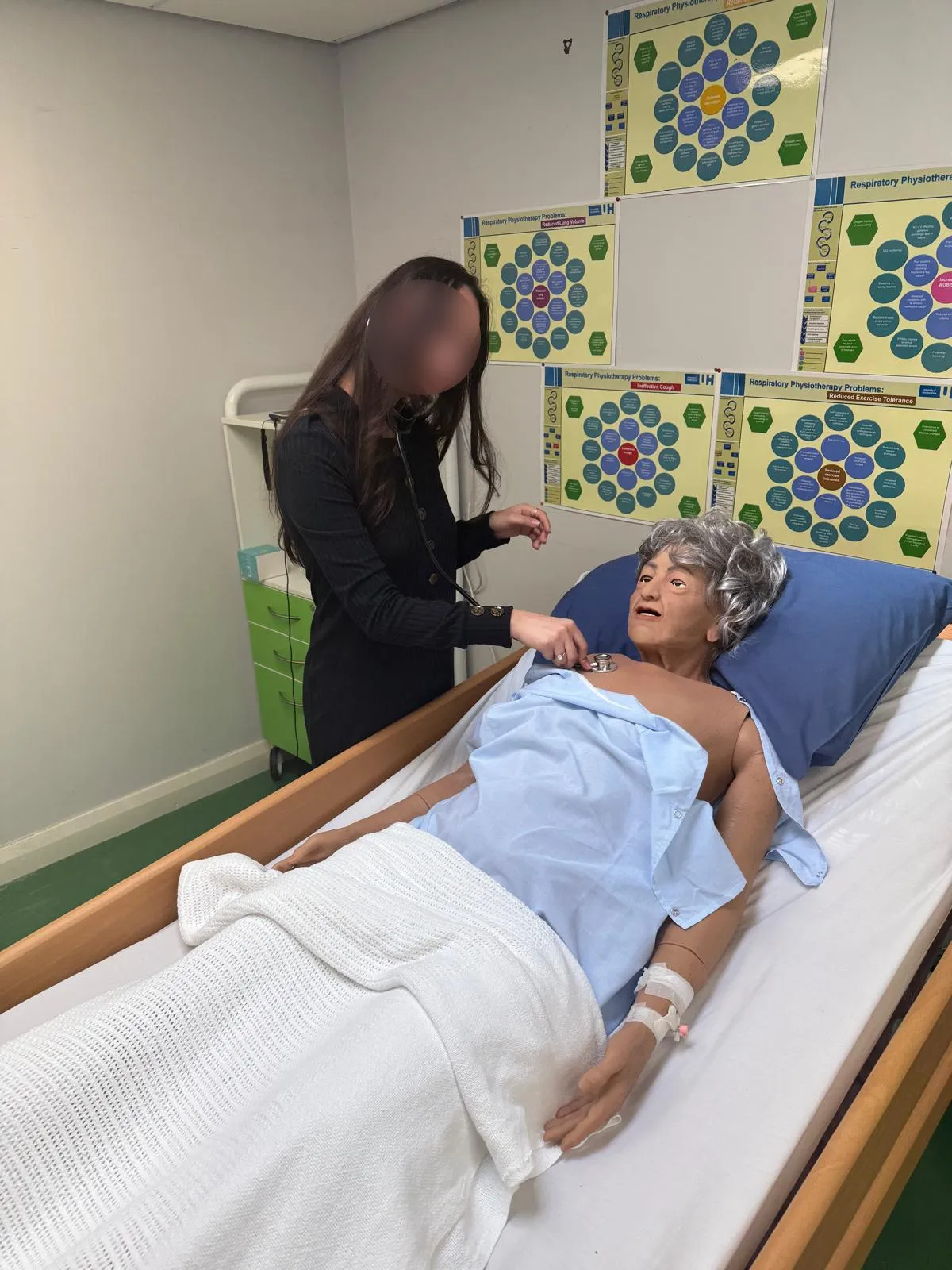 Nour, her face covered, examining a training mannequin during her clinical training.
